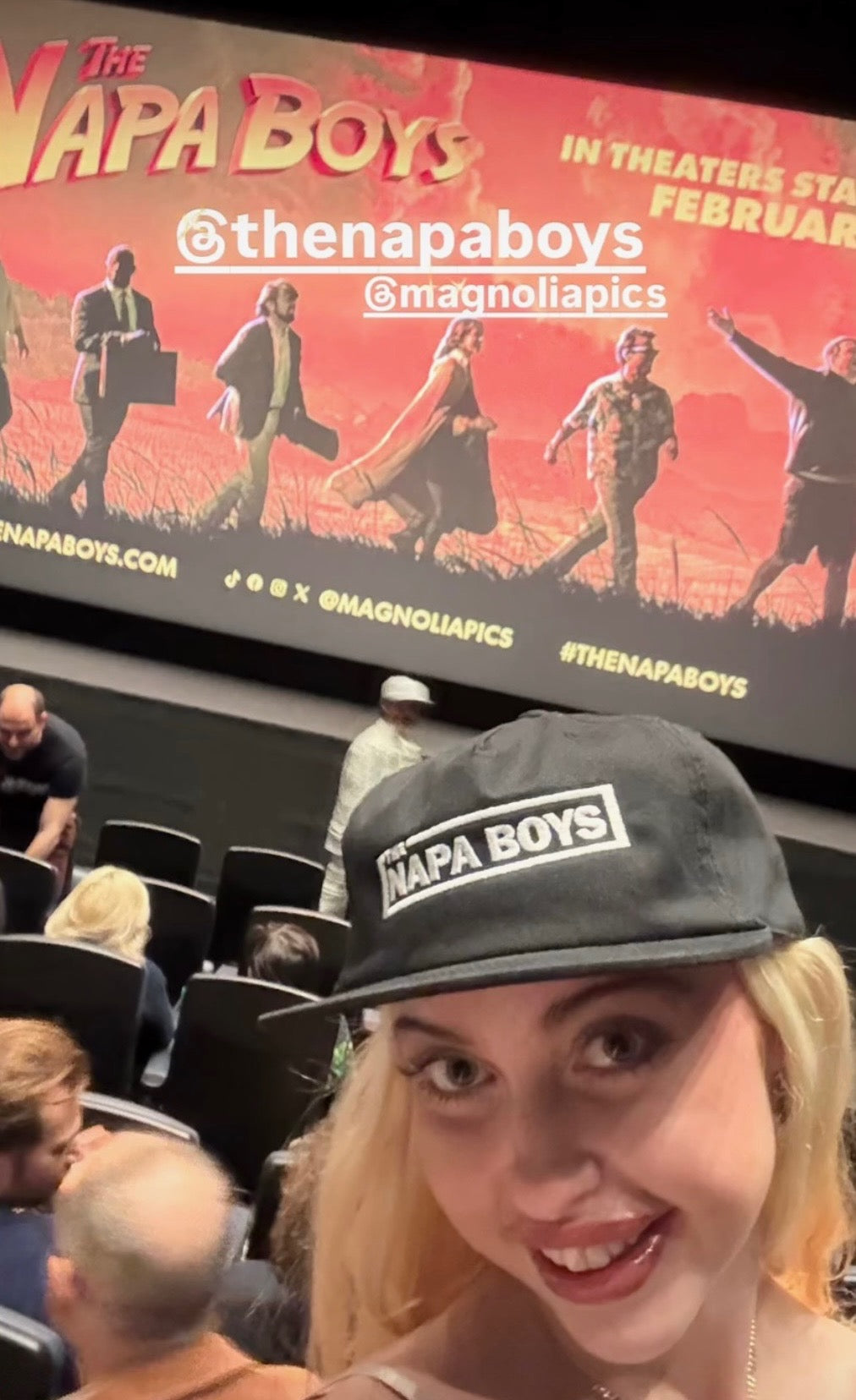 Person wearing a 'Napa Boys' cap in front of a movie theater screen displaying the same title.